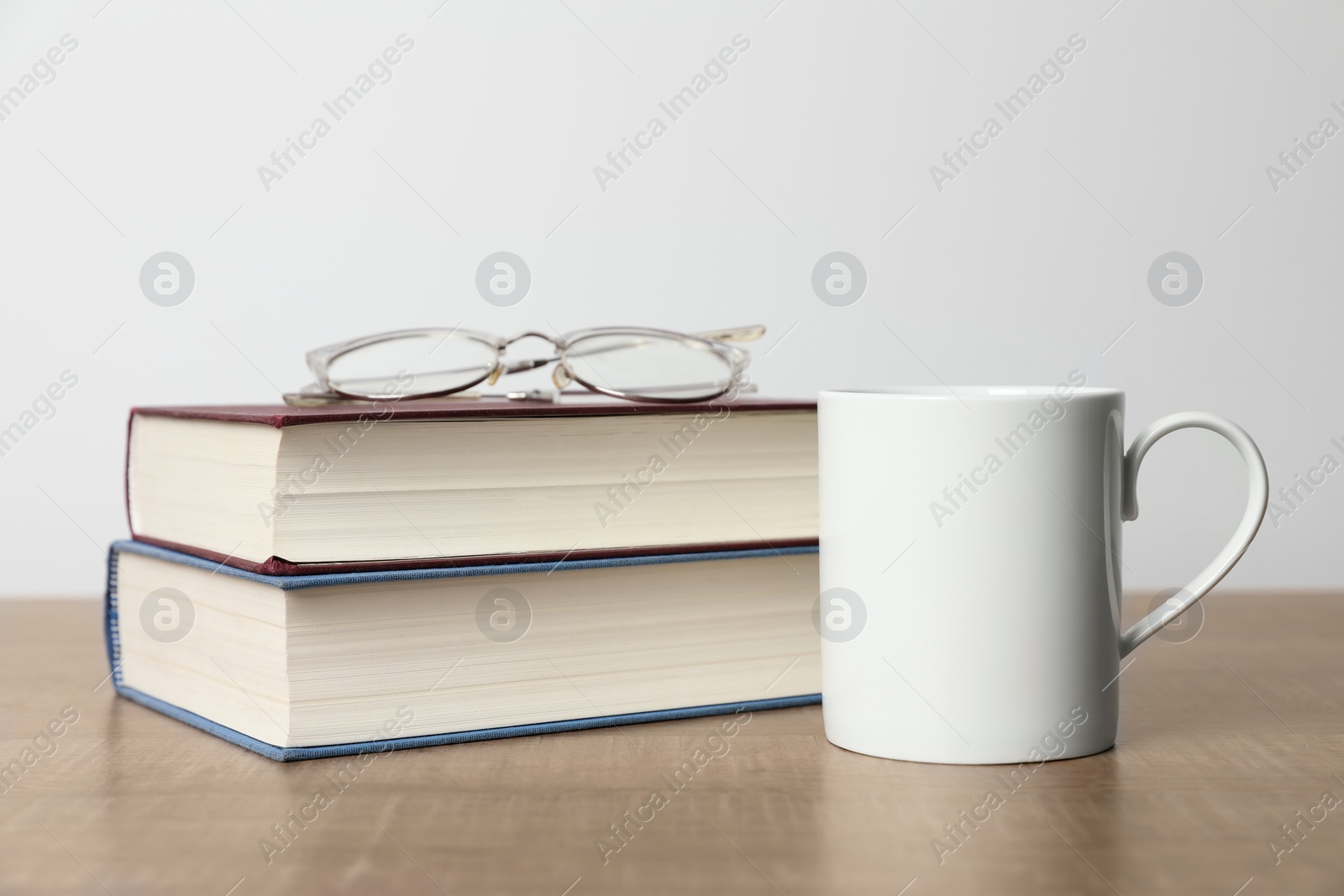 White ceramic mug, stack of books and glasses on wooden table Photo of White ceramic mug, stack of books and glasses on wooden table