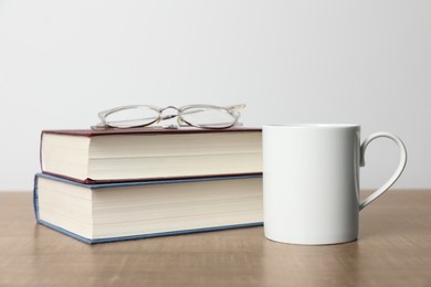 Photo of White ceramic mug, stack of books and glasses on wooden table