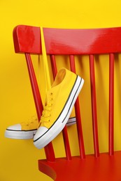 Photo of Pair of sneakers hanging on chair near yellow wall
