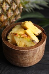 Photo of Pieces of tasty ripe pineapple in bowl on dark wooden table, closeup