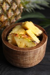 Pieces of tasty ripe pineapple in bowl on dark wooden table, closeup