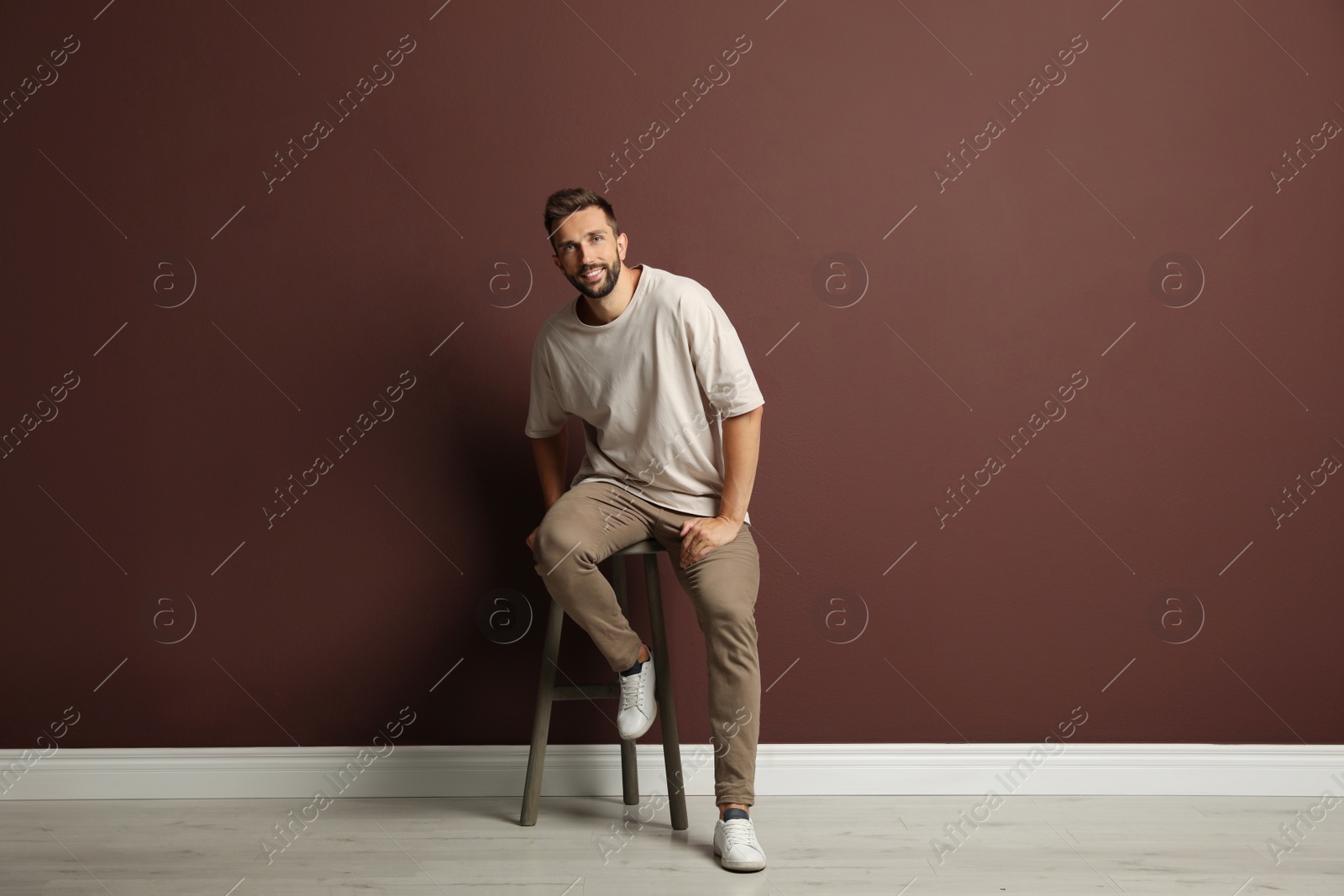 Photo of Handsome man sitting on stool near brown wall