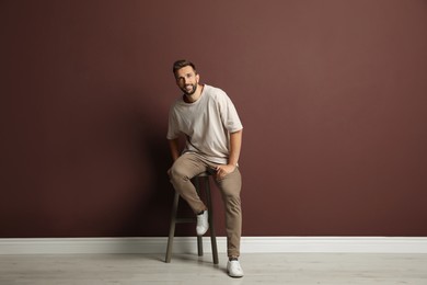Handsome man sitting on stool near brown wall