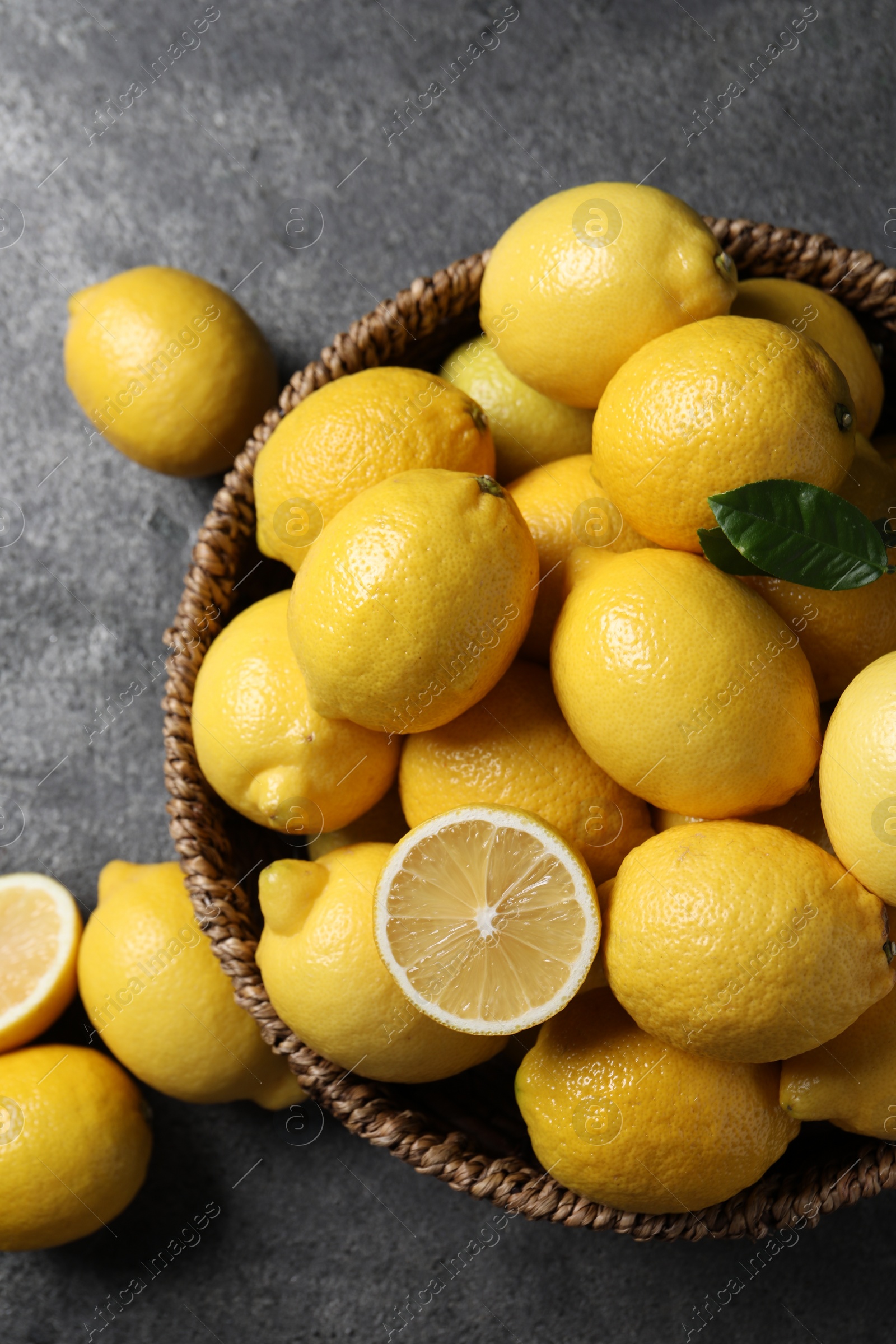 Photo of Fresh lemons in wicker basket on grey table, top view