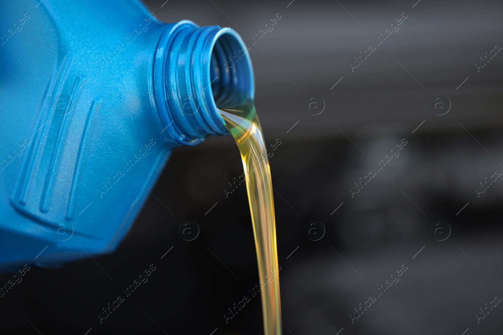 Photo of Pouring motor oil from blue container against blurred background, closeup. Space for text