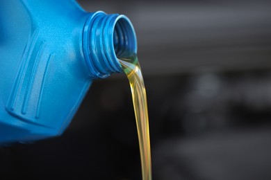 Pouring motor oil from blue container against blurred background, closeup. Space for text