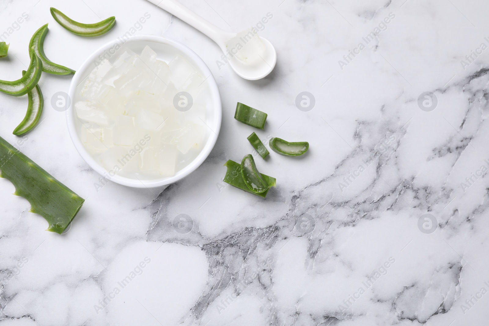 Photo of Aloe vera gel and slices of plant on white marble table, flat lay. Space for text