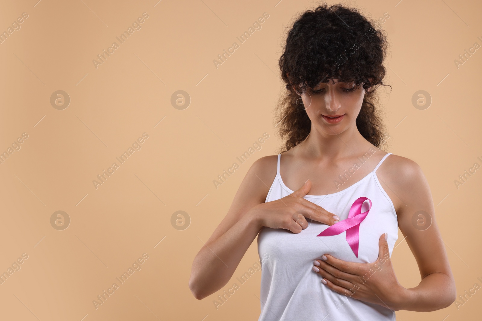 Photo of Breast cancer awareness. Beautiful young woman with pink ribbon doing self-examination on light brown background. Space for text