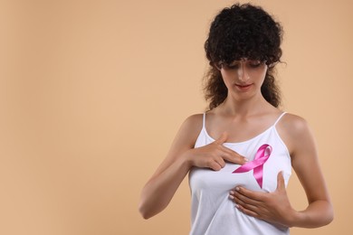 Breast cancer awareness. Beautiful young woman with pink ribbon doing self-examination on light brown background. Space for text