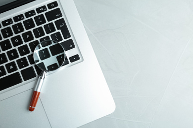 Photo of Magnifying glass and modern laptop on light grey table, space for text. Search concept