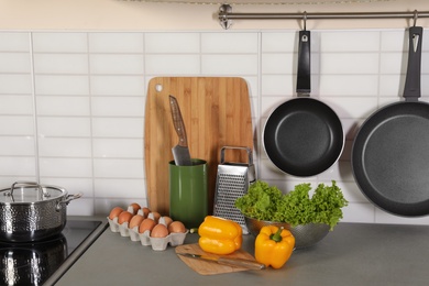 Photo of Set of clean cookware, utensils and products on table in modern kitchen