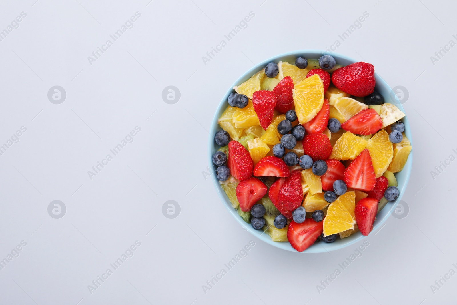 Photo of Yummy fruit salad in bowl on light grey background, top view. Space for text