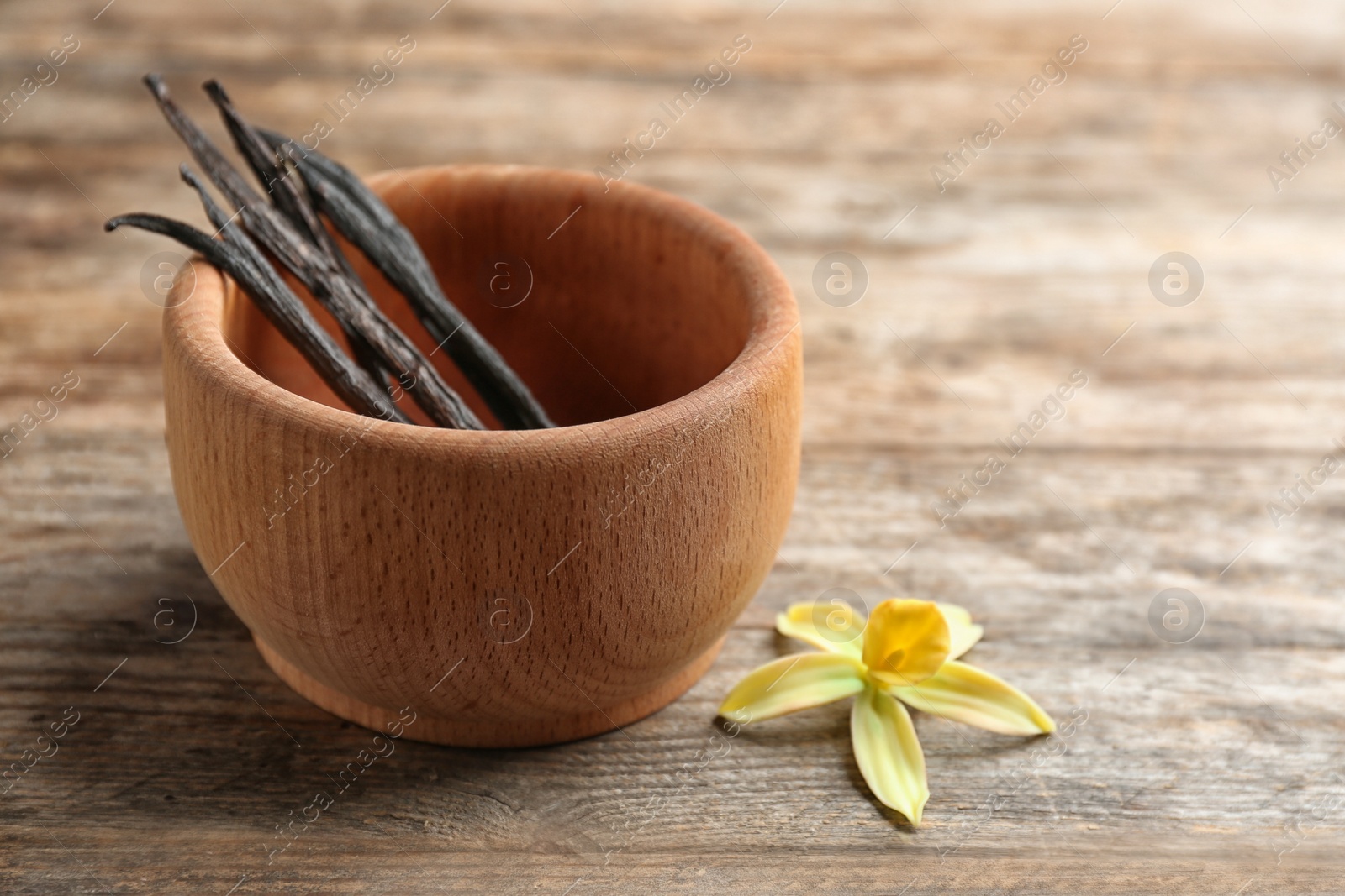 Photo of Flower and bowl with vanilla sticks on wooden background. Space for text