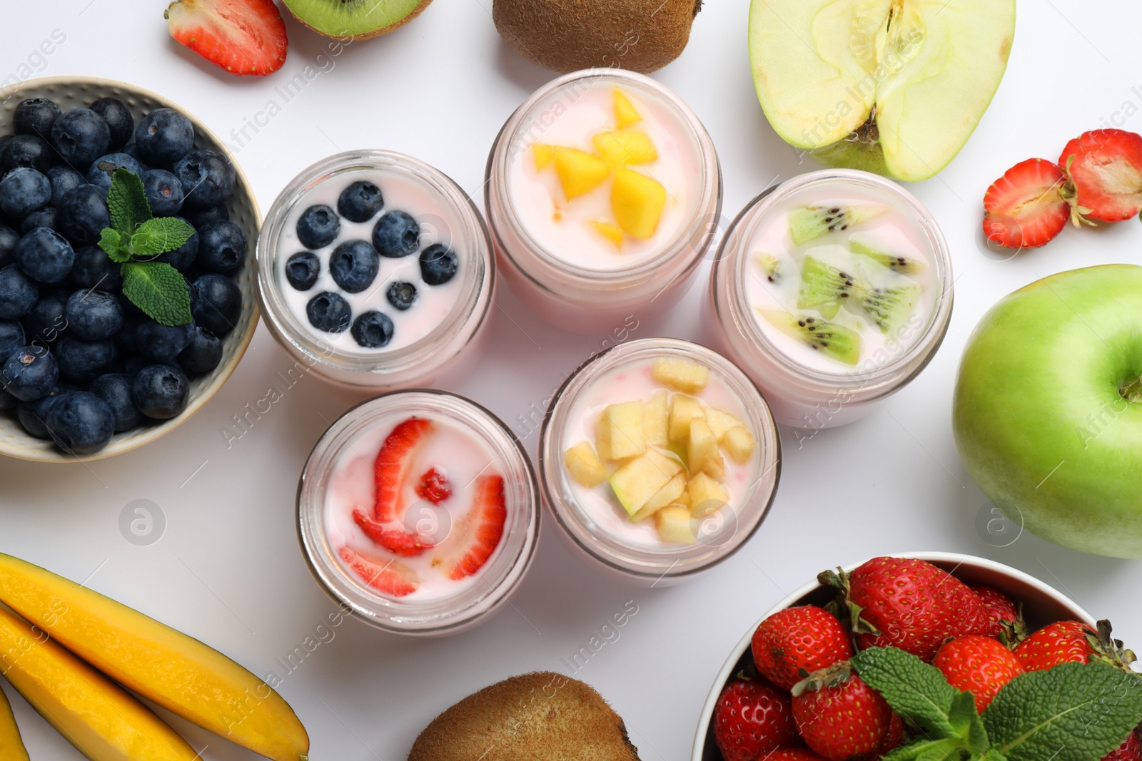 Photo of Tasty yogurt in glass jars and ingredients on white background, top view