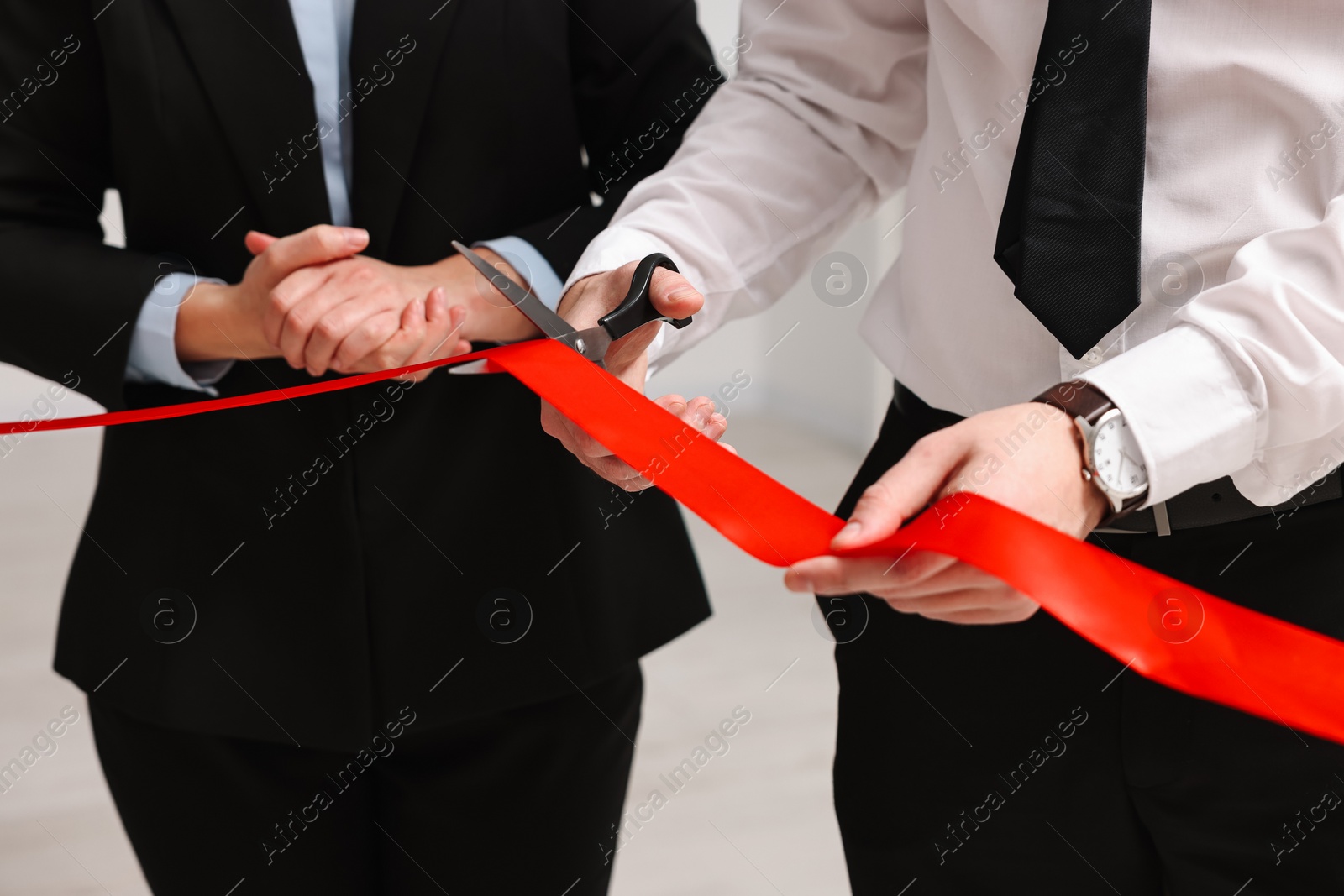 Photo of People cutting red ribbon with scissors on blurred background, closeup