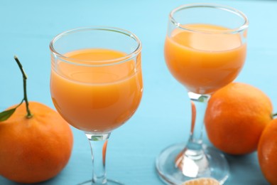 Photo of Delicious tangerine liqueur and fresh fruits on light blue table, closeup