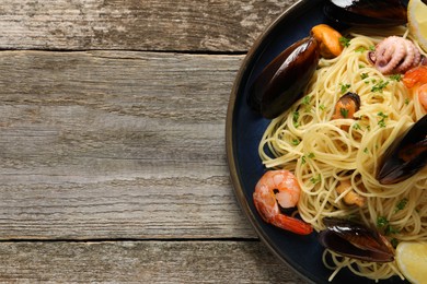 Photo of Delicious spaghetti with seafood served on wooden table, top view. Space for text