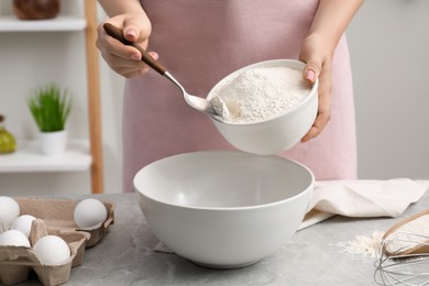 Photo of Preparing tasty baklava. Woman putting flour into bowl at light grey marble table, closeup