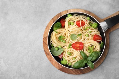 Photo of Delicious pasta primavera in frying pan and ingredients on light gray table, top view. Space for text