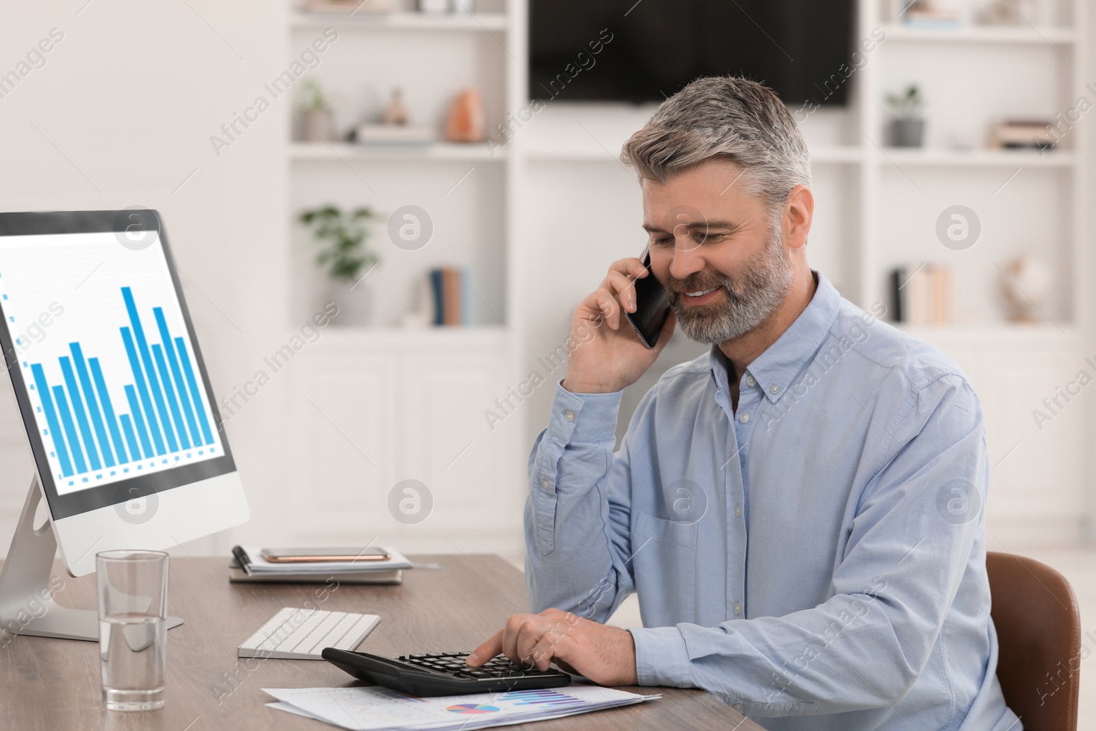 Photo of Professional accountant talking on phone and working at wooden desk in office