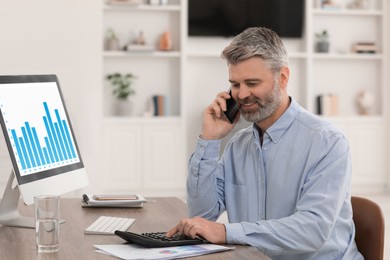 Professional accountant talking on phone and working at wooden desk in office