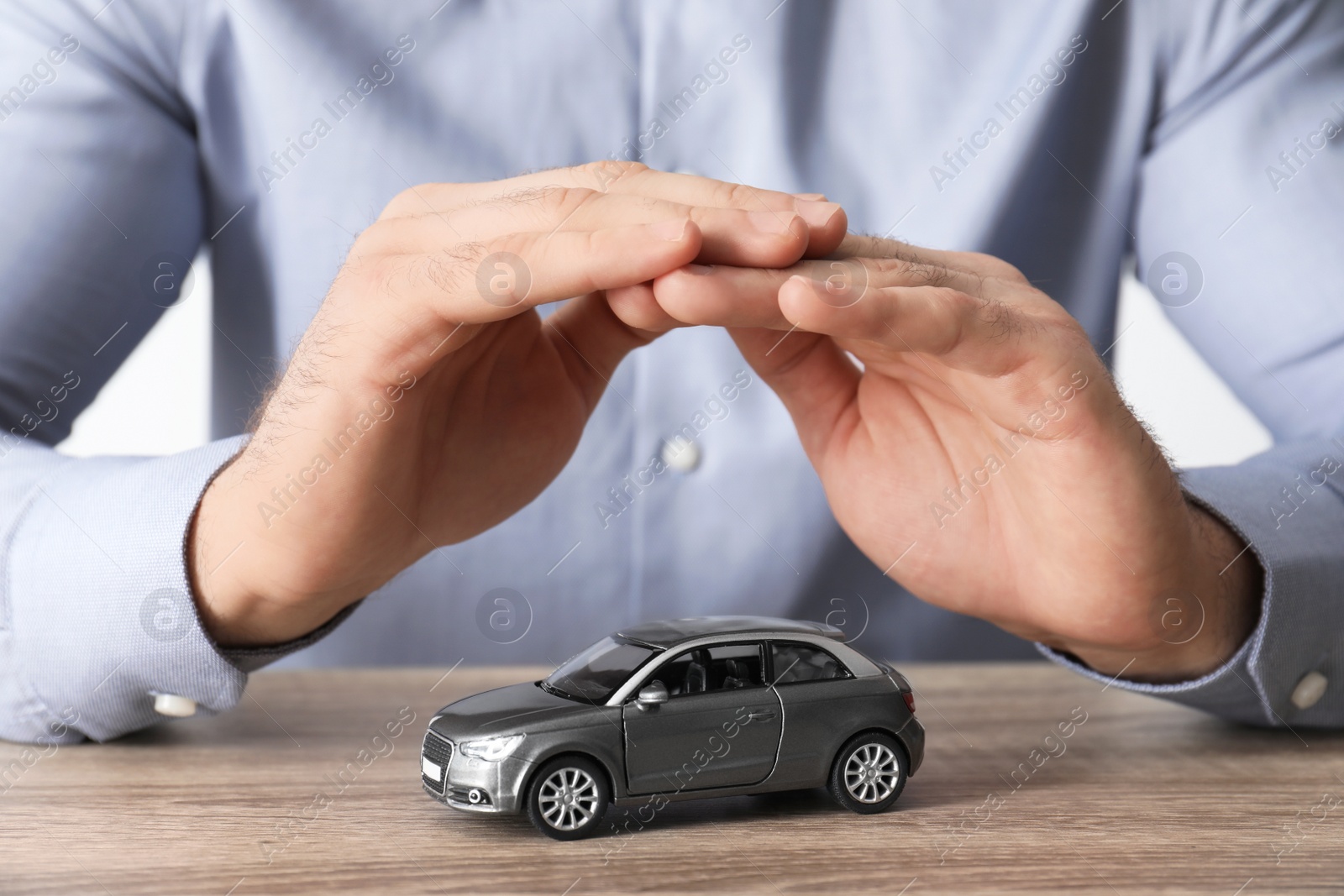 Photo of Male insurance agent covering toy car at table, closeup