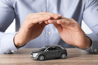 Photo of Male insurance agent covering toy car at table, closeup