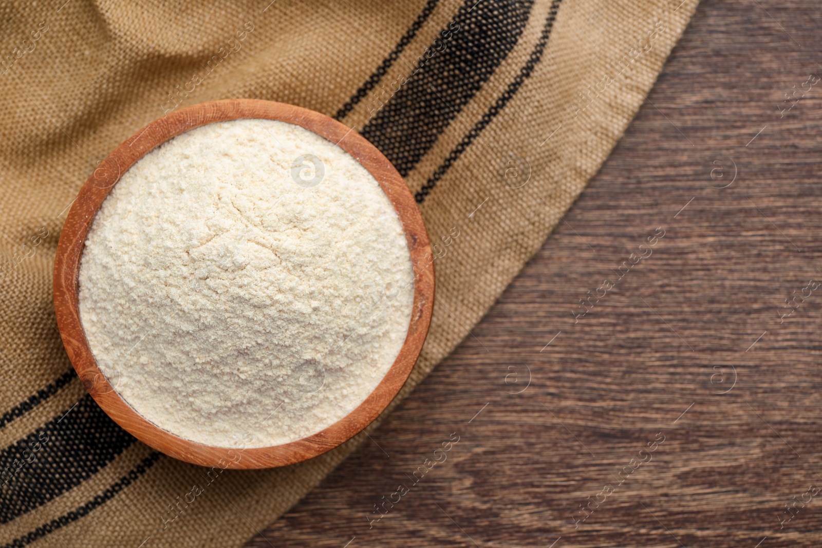 Photo of Organic quinoa flour in bowl on wooden table, top view. Space for text