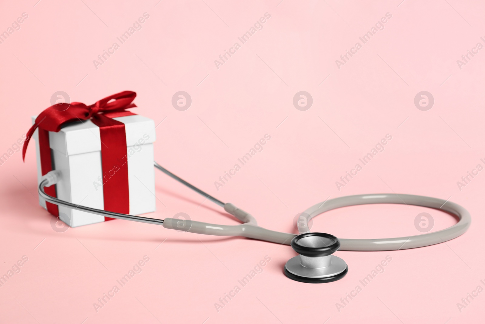 Photo of Stethoscope and gift box on pink background. Happy Doctor's Day