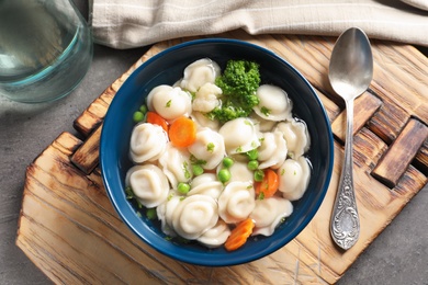 Photo of Board with bowl of dumplings in broth and spoon on table, top view