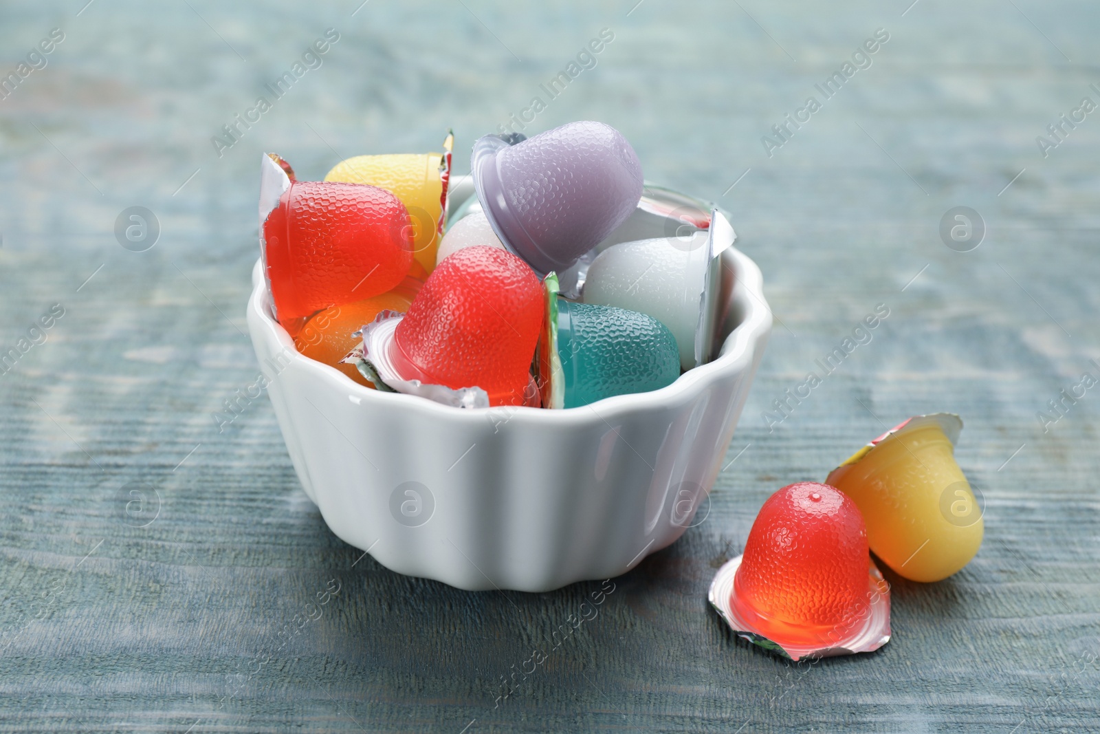 Photo of Bowl with tasty bright jelly cups on light blue wooden table