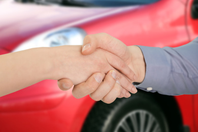 Image of Woman buying car and shaking hands with salesman against blurred auto, closeup