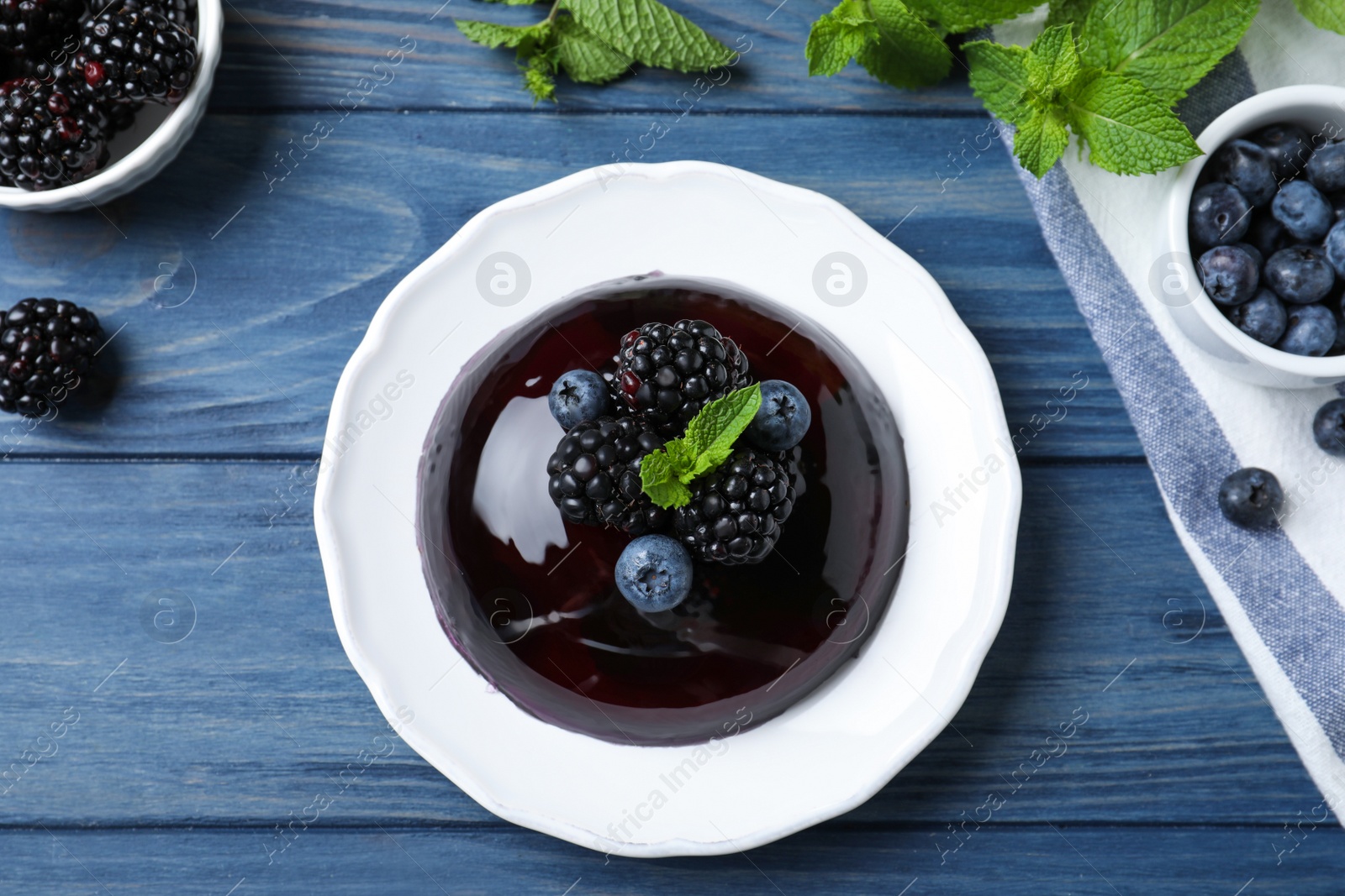 Photo of Delicious fresh jelly with berries on blue wooden table, flat lay