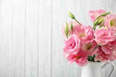 Photo of Eustoma flowers in vase near white wall, space for text