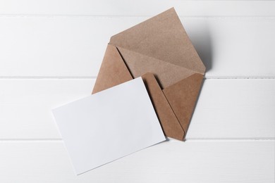 Blank sheet of paper and letter envelope on white wooden table, top view. Space for text