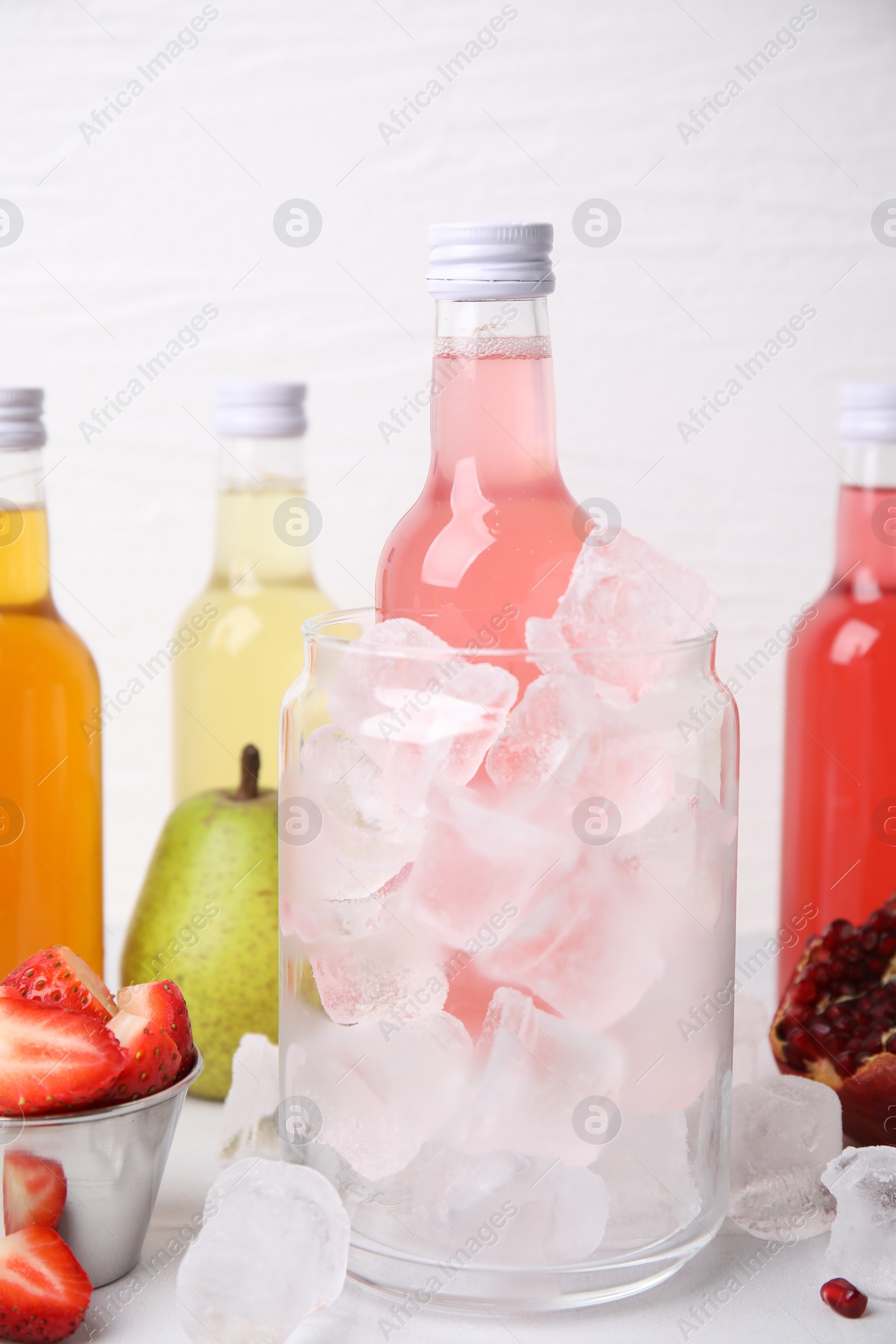 Photo of Tasty kombucha in bottles, glass with ice and fresh fruits on white table