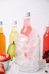 Tasty kombucha in bottles, glass with ice and fresh fruits on white table