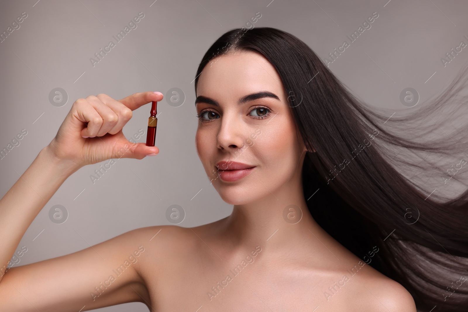 Photo of Beautiful young woman with long healthy hair holding ampoule on grey background