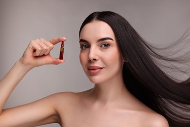 Photo of Beautiful young woman with long healthy hair holding ampoule on grey background