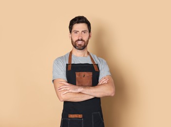 Smiling hairdresser wearing apron on light brown background