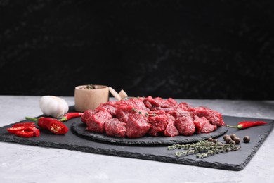 Photo of Pieces of raw beef meat, products and spices on grey textured table against black background. Space for text
