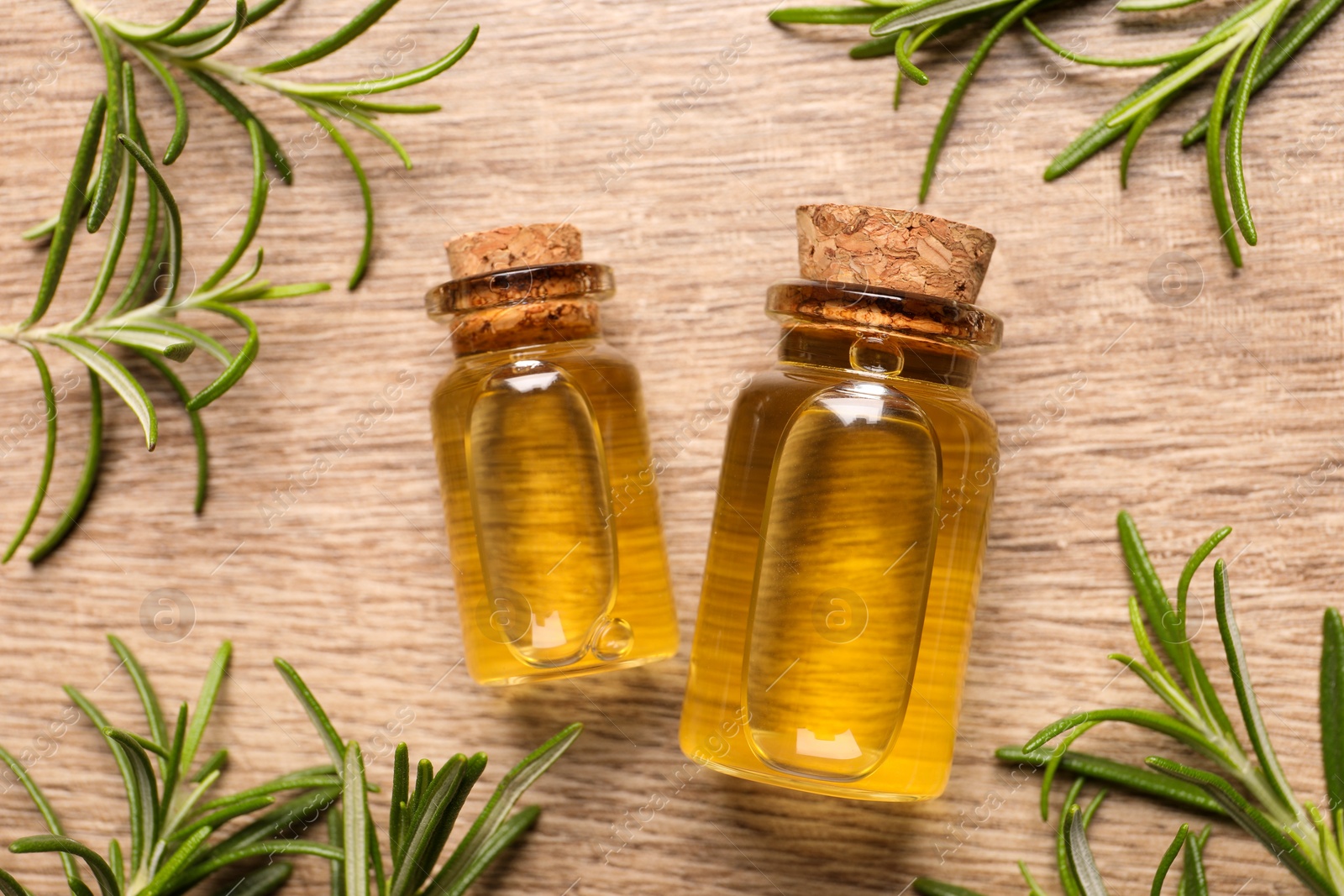 Photo of Bottles with essential oil and fresh rosemary on wooden table, flat lay