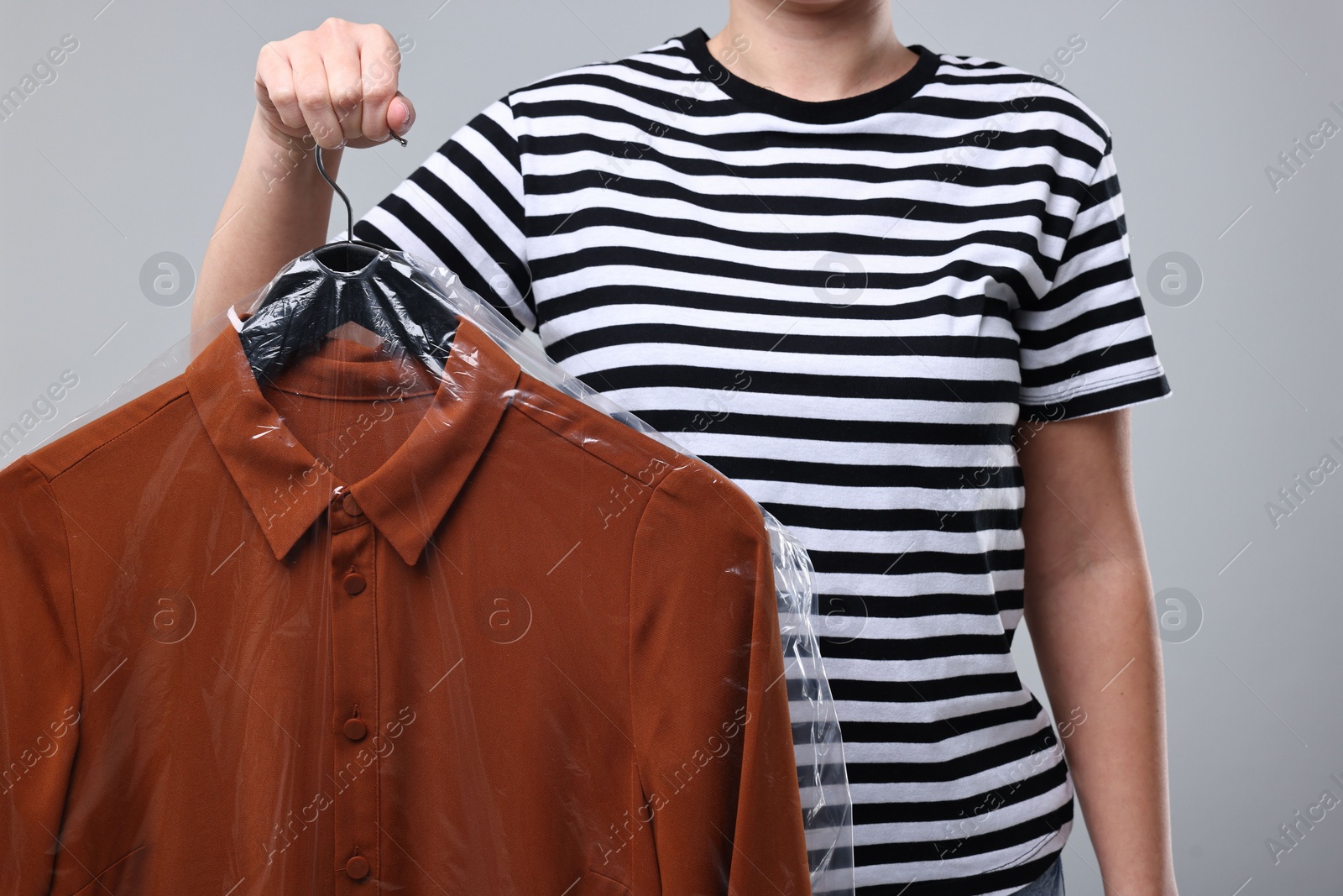 Photo of Dry-cleaning service. Woman holding shirt in plastic bag on gray background, closeup