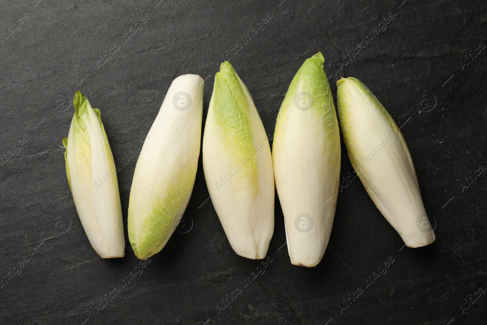 Photo of Fresh raw Belgian endives (chicory) on black table, top view