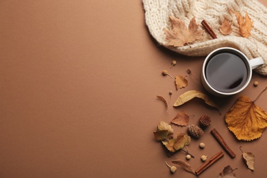 Flat lay composition with cup of hot drink and autumn leaves on brown background, space for text. Cozy atmosphere