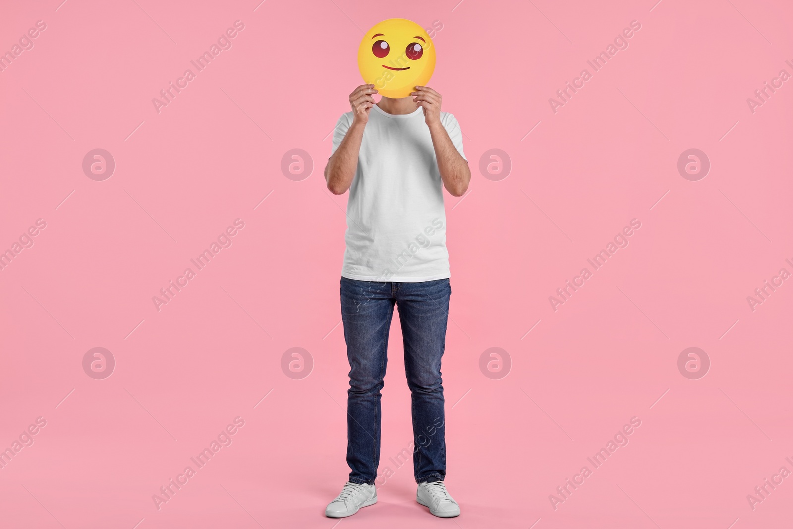 Photo of Man covering face with smiling emoticon on pink background