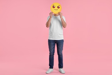 Photo of Man covering face with smiling emoticon on pink background