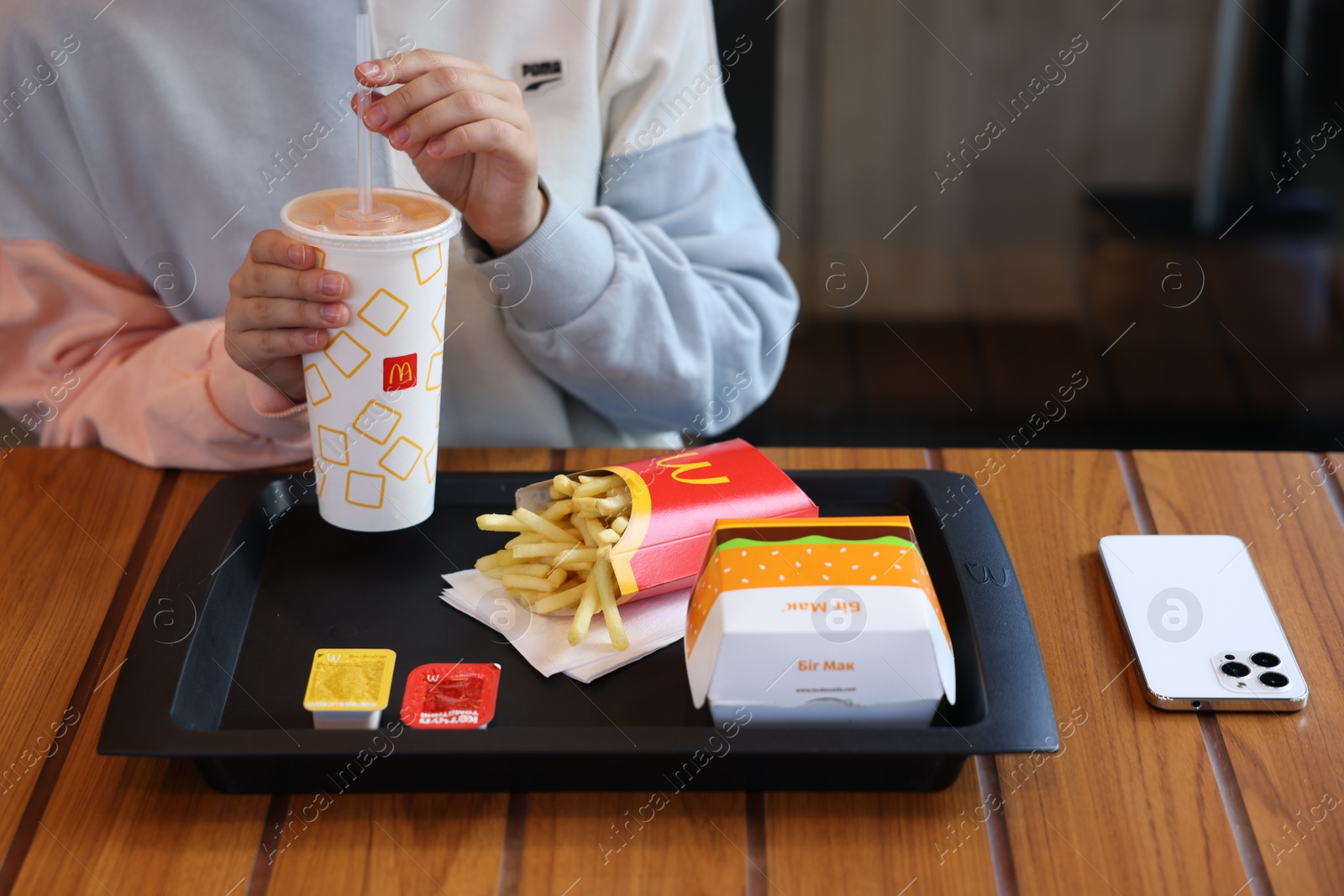 Photo of Lviv, Ukraine - September 26, 2023: Woman with McDonald's drink, burger and french fries at wooden table in restaurant, closeup