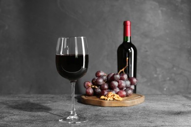 Glass of red wine, bottle, nuts and grapes on grey table
