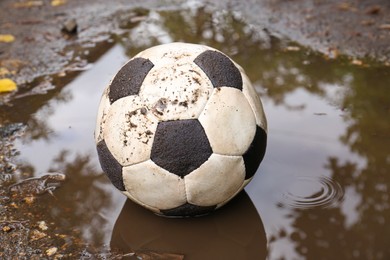 Dirty soccer ball in muddy puddle outdoors
